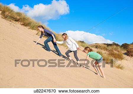 Stock Image - Three girls climbing up sand dune. Fotosearch