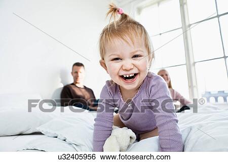 Toddler girl on parent's bed looking at camera, laughing View Large Photo Image Stock Photograph - Toddler girl on parent's bed looking at camera, laughing. Fotosearch
