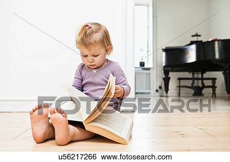 Stock Photograph - Toddler girl sitting on floor reading book. Fotosearch