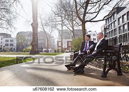 Two businessmen sitting on park bench View Large Photo Image Stock Image - Two businessmen sitting on park bench. Fotosearch