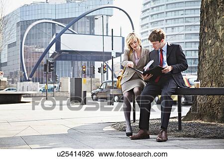 Stock Photograph - Two businesspeople sitting on railing in city. Fotosearch
