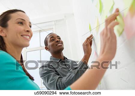 Two colleagues sticking adhesive notes to wall View Large Photo Image Picture - Two colleagues sticking adhesive notes to wall. Fotosearch