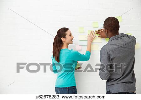 Two colleagues sticking adhesive notes to wall View Large Photo Image Stock Image - Two colleagues sticking adhesive notes to wall. Fotosearch