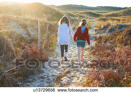 Two girls walking on path in sand dunes rear view View Large Photo Image Stock Photograph - Two girls walking on path in sand dunes rear view. Fotosearch