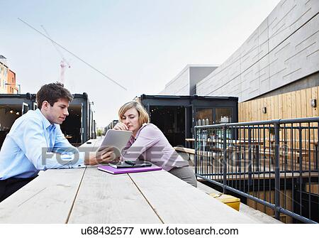 Stock Photo - Two people sitting at table using digital tablet outdoors. Fotosearch
