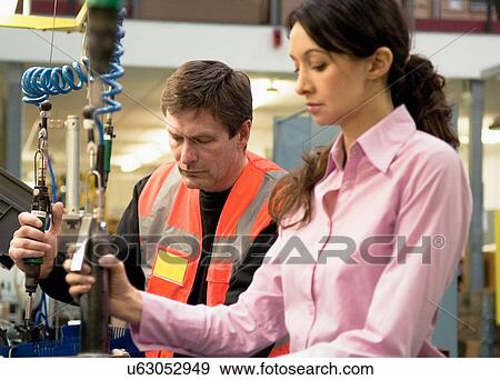 Stock Photo - Woman and man working on machinery in electrical component factory. Fotosearch