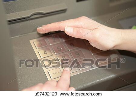 Stock Photo - Woman covering keypad when entering PIN in cashpoint. Fotosearch