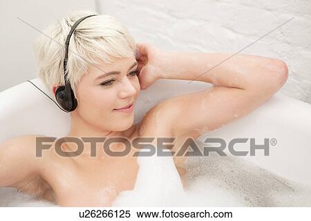 Stock Photography - Woman in bubble bath wearing earphones. Fotosearch