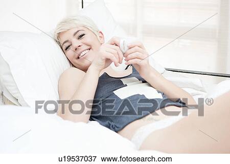 Woman lying on bed holding teacup View Large Photo Image Stock Photo - Woman lying on bed holding teacup. Fotosearch