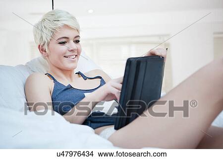 Woman lying on bed using digital tablet View Large Photo Image Picture - Woman lying on bed using digital tablet. Fotosearch