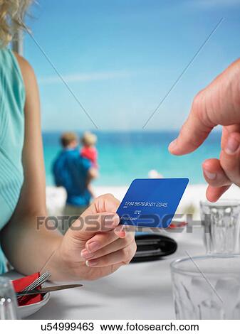 Stock Image - Woman paying beach restaurant with credit card. Fotosearch