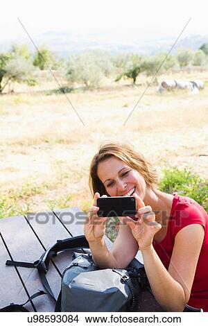 Woman sitting at picnic bench photographing self with camera phone View Large Photo Image Picture - Woman sitting at picnic bench photographing self with camera phone. Fotosearch