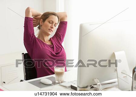 Picture - Woman stretching with eyes closed at desk. Fotosearch