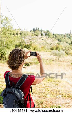 Stock Image - Woman taking photo of rural scene on camera phone. Fotosearch