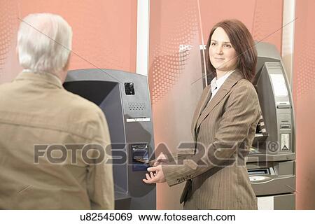 Woman using cashpoint, man waiting View Large Photo Image Stock Photo - Woman using cashpoint, man waiting. Fotosearch