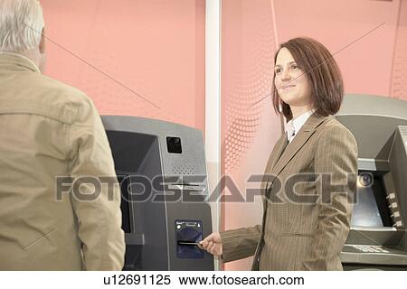 Woman using cashpoint, man waiting View Large Photo Image Stock Photography - Woman using cashpoint, man waiting. Fotosearch