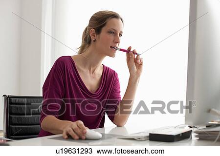 Stock Image - Woman using computer mouse, biting pen. Fotosearch