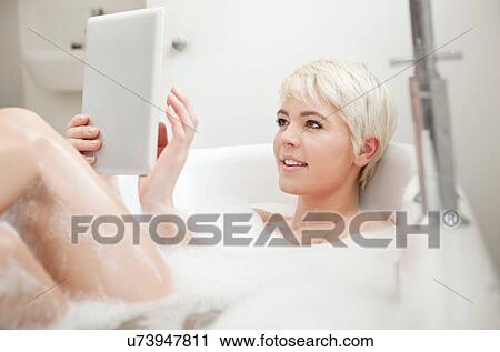 Stock Image - Woman using digital tablet in bubble bath. Fotosearch