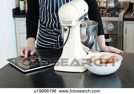 Stock Photo - Woman using digital tablet to check recipe. Fotosearch