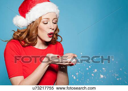 Stock Photography - Woman wearing santa hat blowing snow. Fotosearch