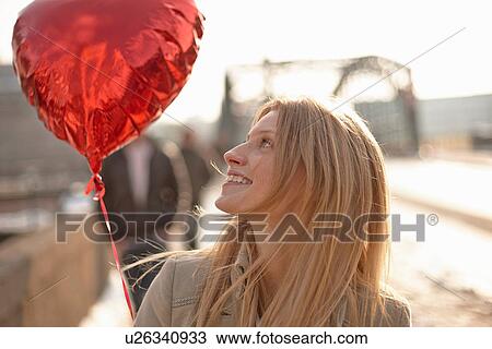 Stock Image - Woman with red heart-shaped balloon. Fotosearch