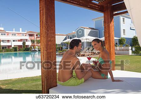 Young couple sitting on sunlounger at holiday resort with cocktails View Large Photo Image Picture - Young couple sitting on sunlounger at holiday resort with cocktails. Fotosearch