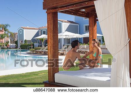 Stock Photo - Young couple sitting on sunlounger at holiday resort. Fotosearch