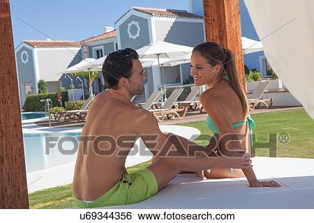 Stock Photograph - Young couple sitting on sunlounger at holiday resort. Fotosearch