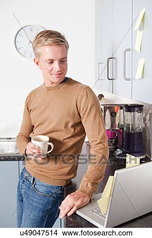 Young man in kitchen with coffee cup and laptop View Large Photo Image Picture - Young man in kitchen with coffee cup and laptop. Fotosearch