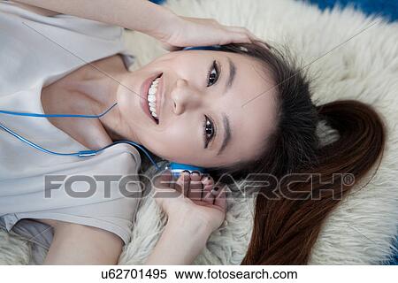 Young woman lying on rug wearing headphones View Large Photo Image Stock Photography - Young woman lying on rug wearing headphones. Fotosearch