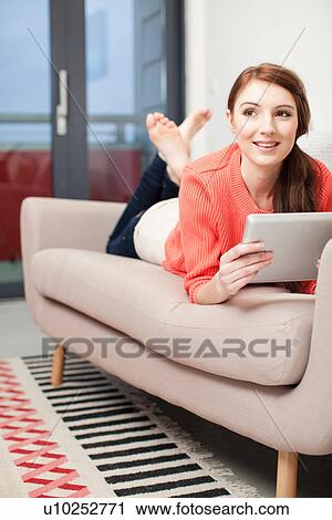 Stock Image - Young woman lying on sofa using digital tablet. Fotosearch