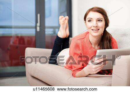 Stock Photo - Young woman lying on sofa using digital tablet. Fotosearch