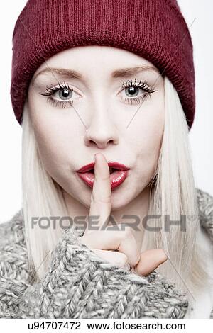 Stock Image - Young woman wearing red hat with finger on lips. Fotosearch