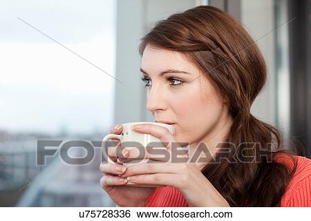 Stock Photograph - Young woman with coffee cup looking out of window. Fotosearch