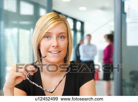 Stock Photo - Blonde woman holding glasses with colleagues in background. Fotosearch