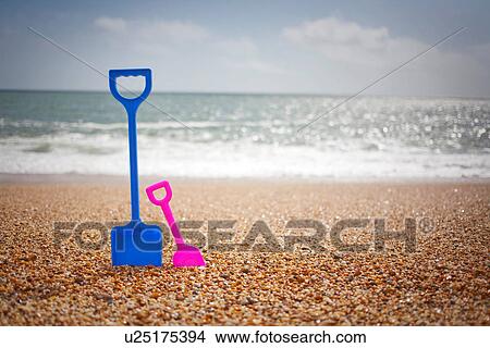 Picture - Blue and pink spades standing in sand at beach. Fotosearch