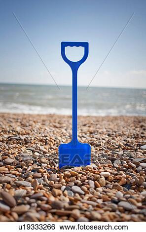 Blue spade stuck into pebbles on beach View Large Photo Image Stock Photograph - Blue spade stuck into pebbles on beach. Fotosearch