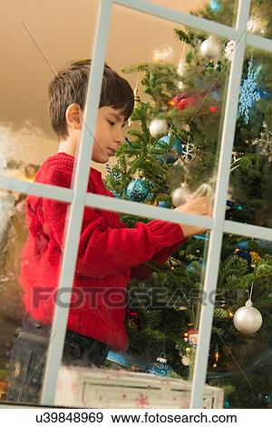 Boy decorating christmas tree in front of window View Large Photo Image Stock Photo - Boy decorating christmas tree in front of window. Fotosearch