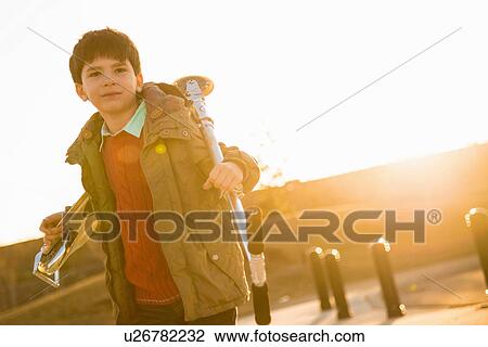 Stock Image - Boy in park carrying scooter. Fotosearch