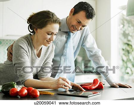 Stock Image - Businessman and wife using digital tablet in kitchen. Fotosearch