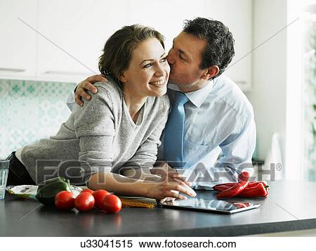 Stock Photography - Businessman kissing wife in kitchen. Fotosearch