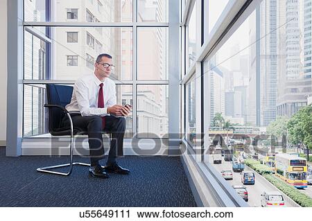 Businessman sitting on chair looking out of office window View Large Photo Image Stock Image - Businessman sitting on chair looking out of office window. Fotosearch