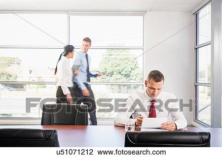 Stock Image - Businessman working at desk, colleagues in background. Fotosearch
