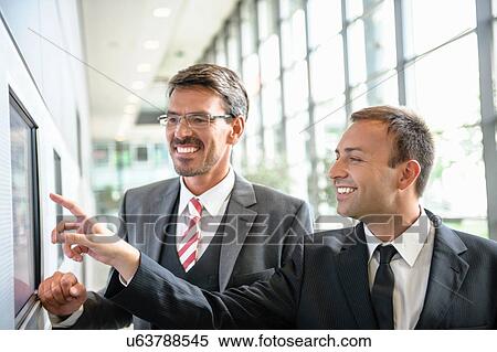 Stock Photography - Businessmen pointing and looking at wall screen. Fotosearch