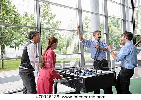 Stock Photography - Businessmen winning at table football in lobby. Fotosearch
