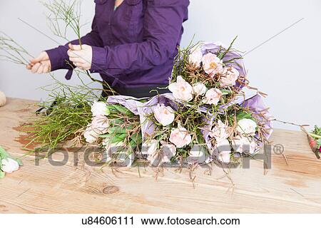 Stock Image - Close up of young florist arranging plants and roses into bouquet. Fotosearch