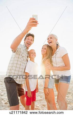 Stock Image - Family photographing themselves on beach. Fotosearch