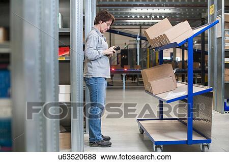Stock Photo - Female warehouse worker checking orders on distribution trolley. Fotosearch