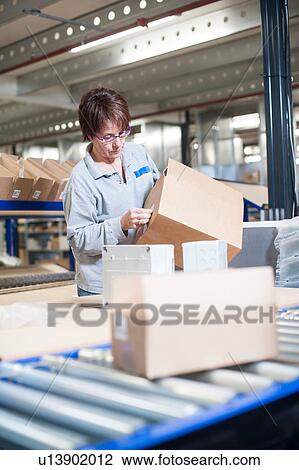 Stock Image - Female warehouse worker labeling box for conveyor belt. Fotosearch