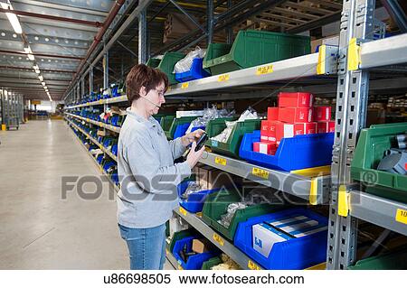 Stock Photography - Female warehouse worker selecting item from shelving. Fotosearch